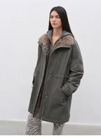 Person wearing a long green coat with fur collar against a white background