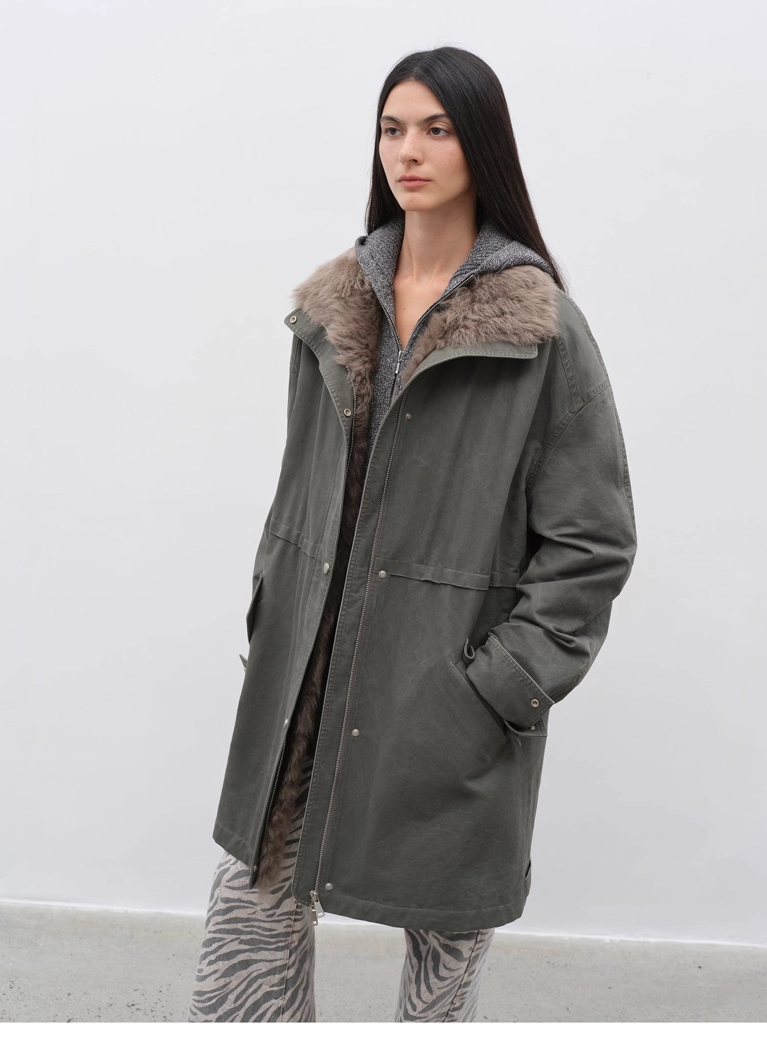 Person wearing a long green coat with fur collar against a white background