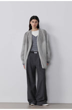 Person wearing a gray cardigan, gray sweater, and gray pants against a white background