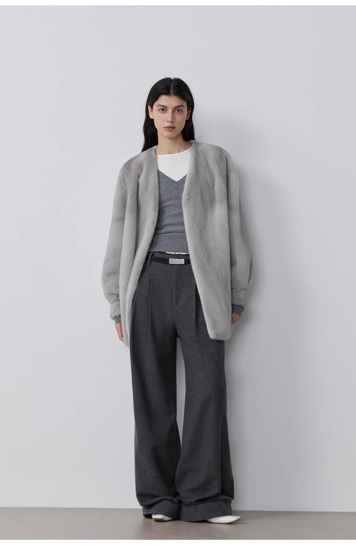 Person wearing a gray cardigan, gray sweater, and gray pants against a white background