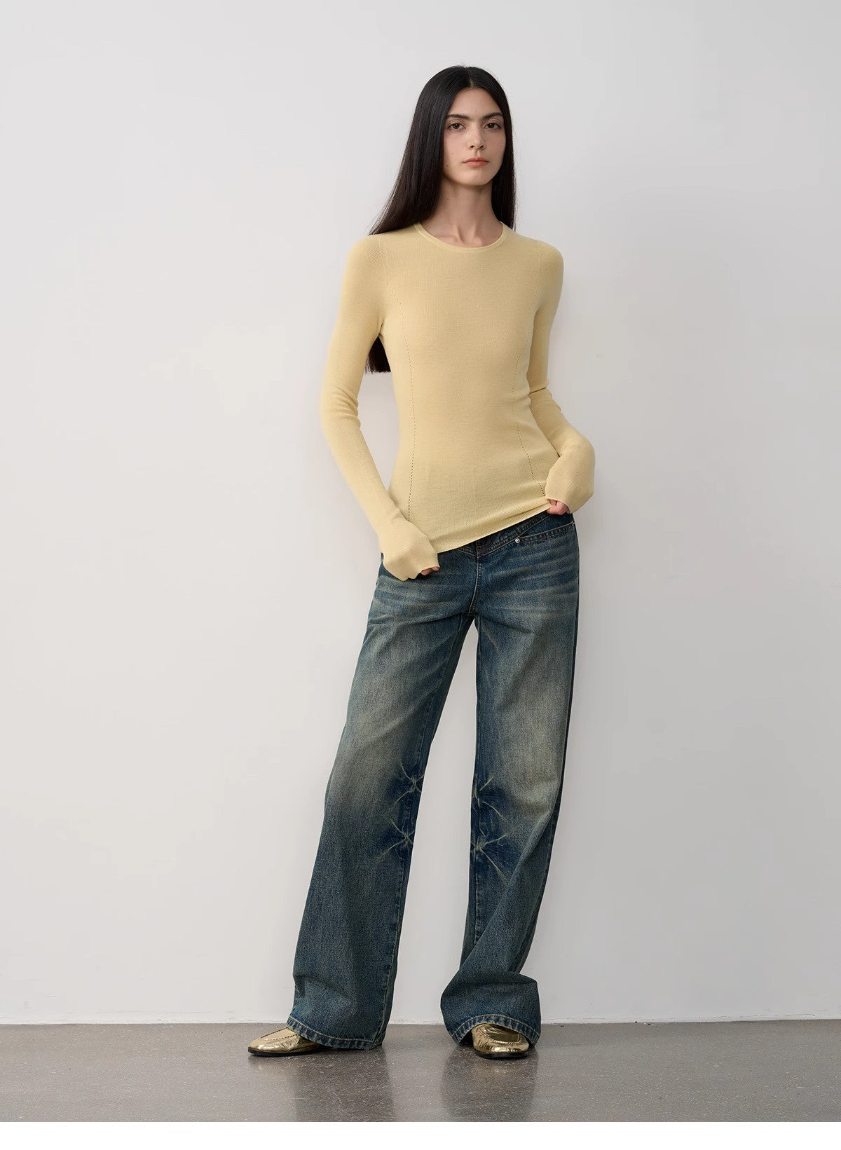Woman wearing a yellow sweater and blue jeans against a white background