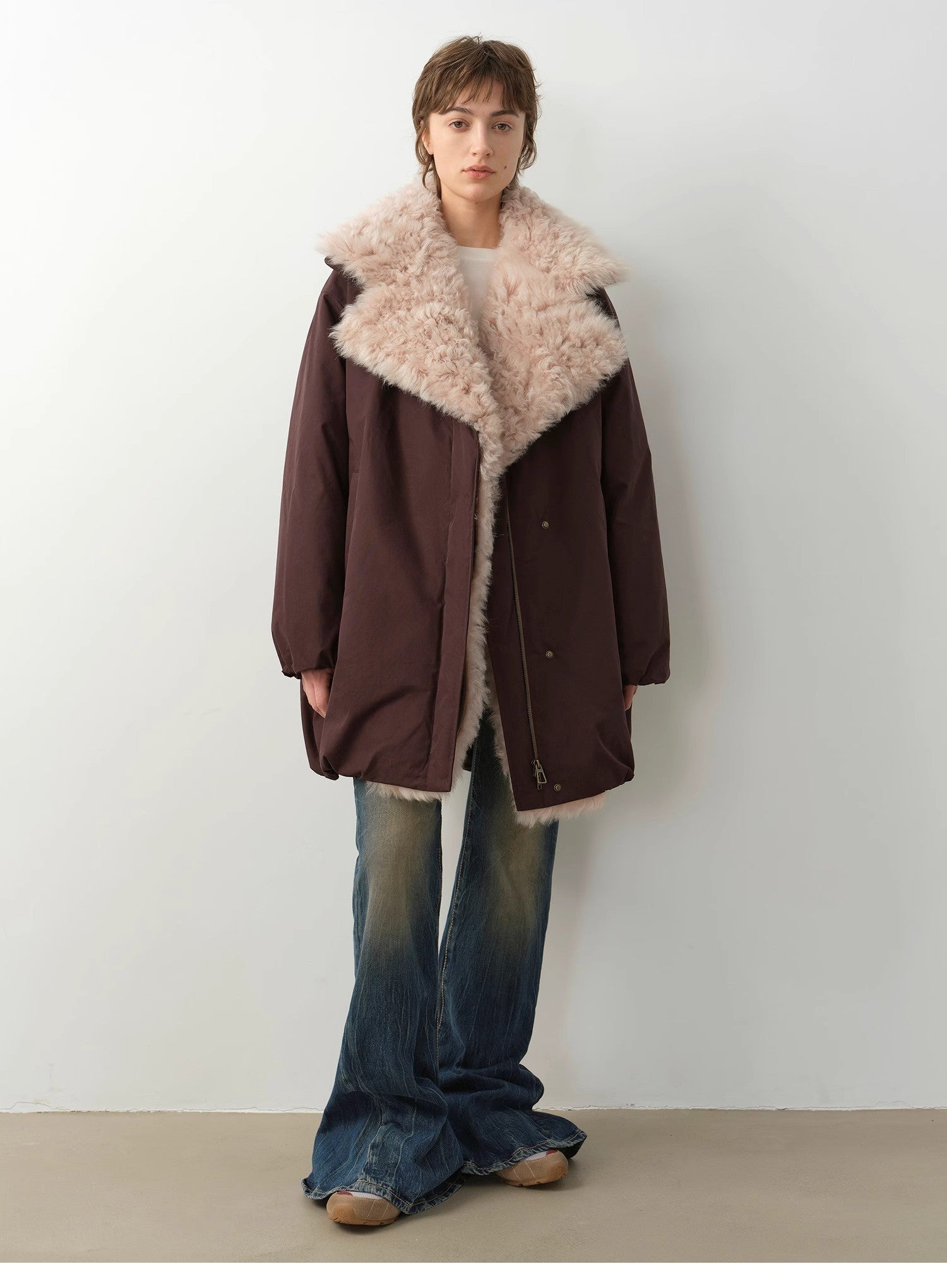 Person wearing a brown coat with a fur-lined hood against a white background