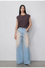 Woman wearing a sleeveless top and gradient jeans against a plain background
