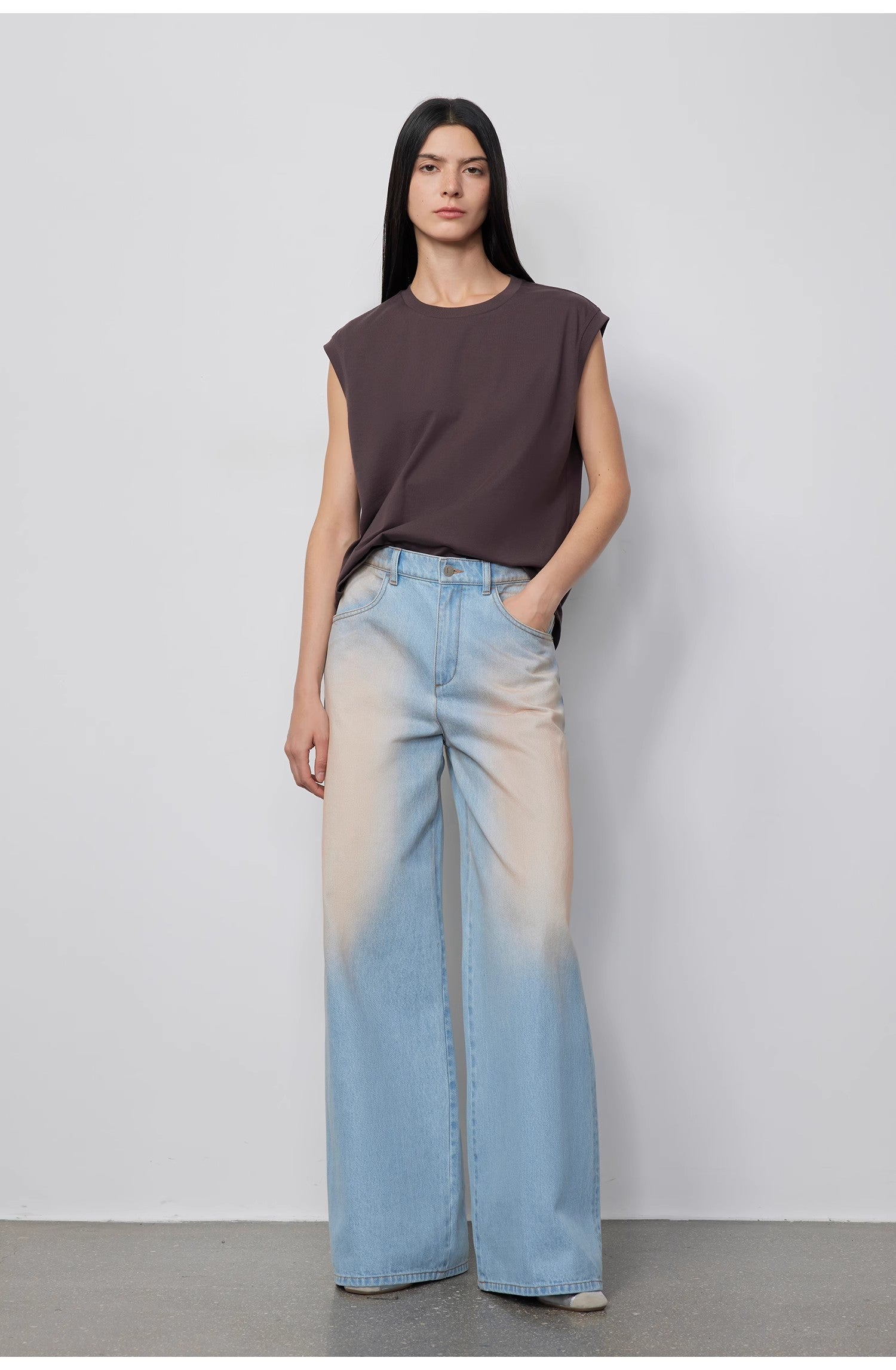 Woman wearing a sleeveless top and gradient jeans against a plain background