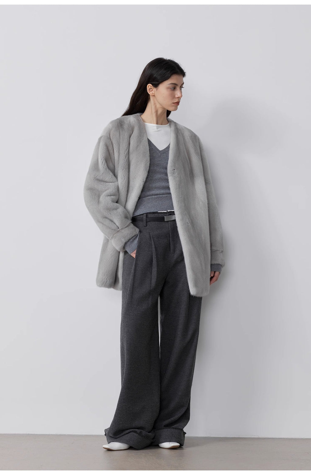 Person wearing a gray coat and dark pants against a white background