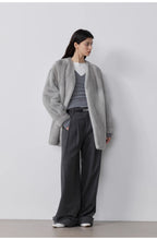 Person wearing a gray coat and dark pants against a white background