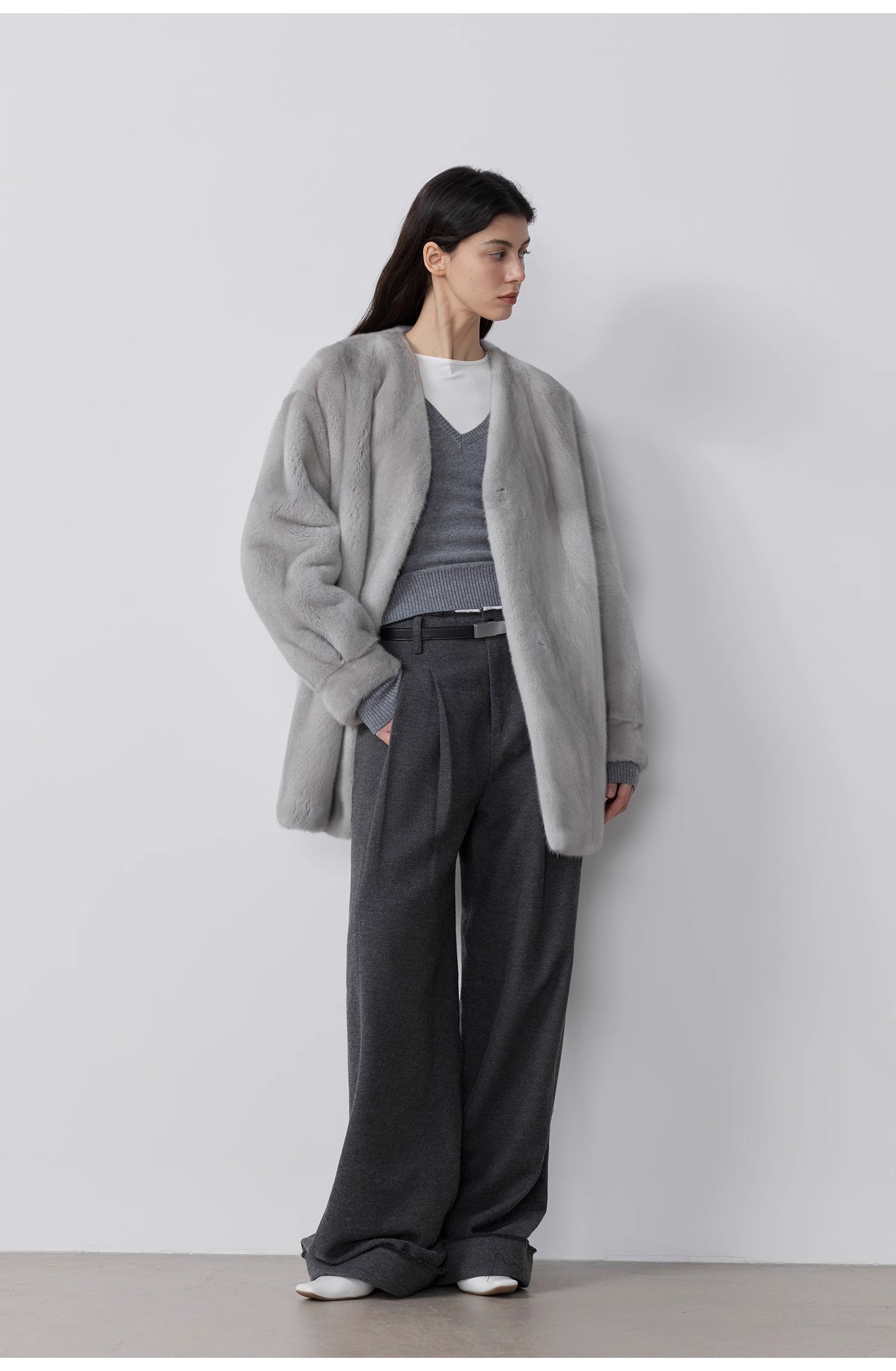 Person wearing a gray coat and dark pants against a white background