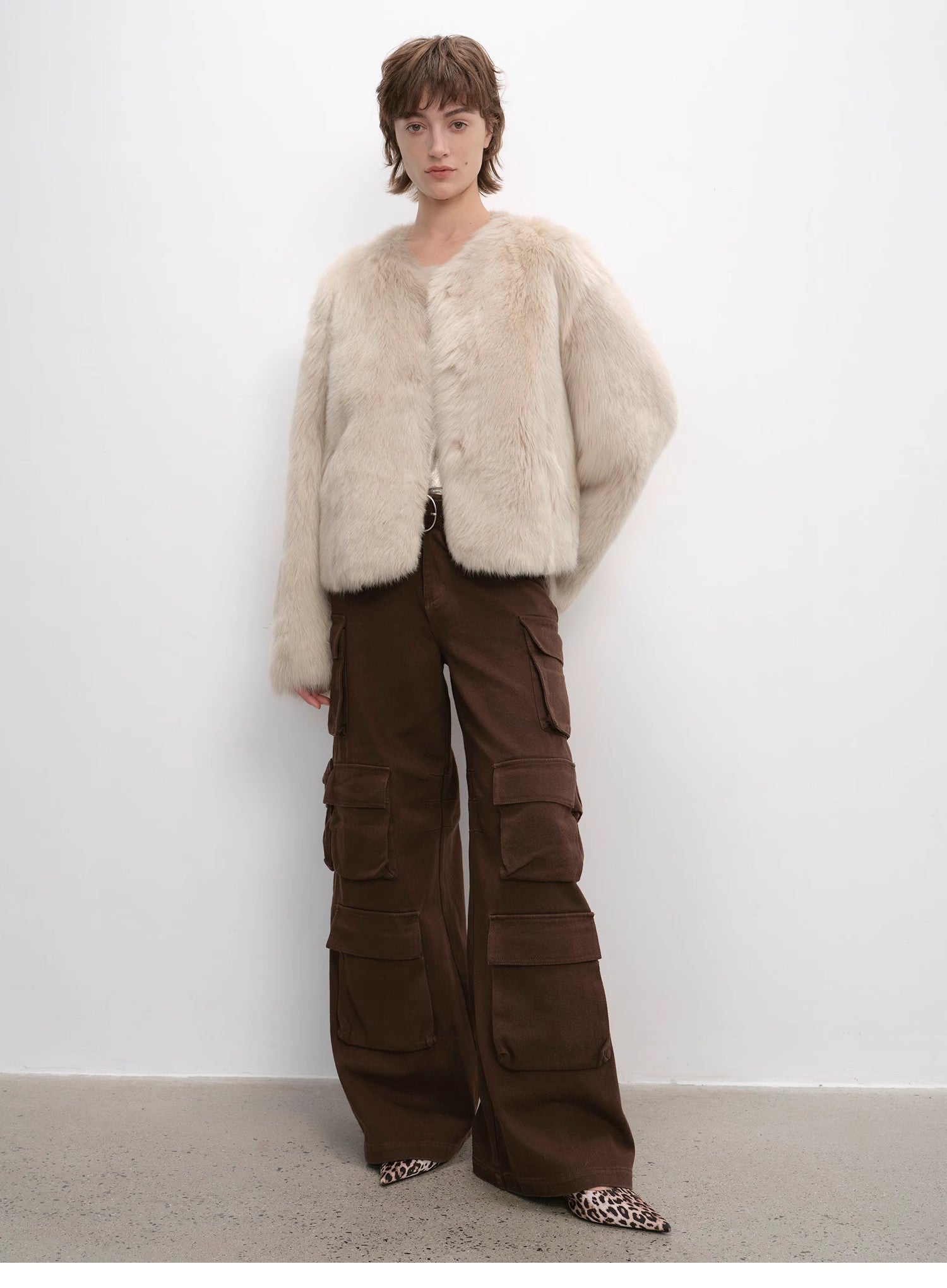 Person wearing a fluffy white coat and brown cargo pants against a white background