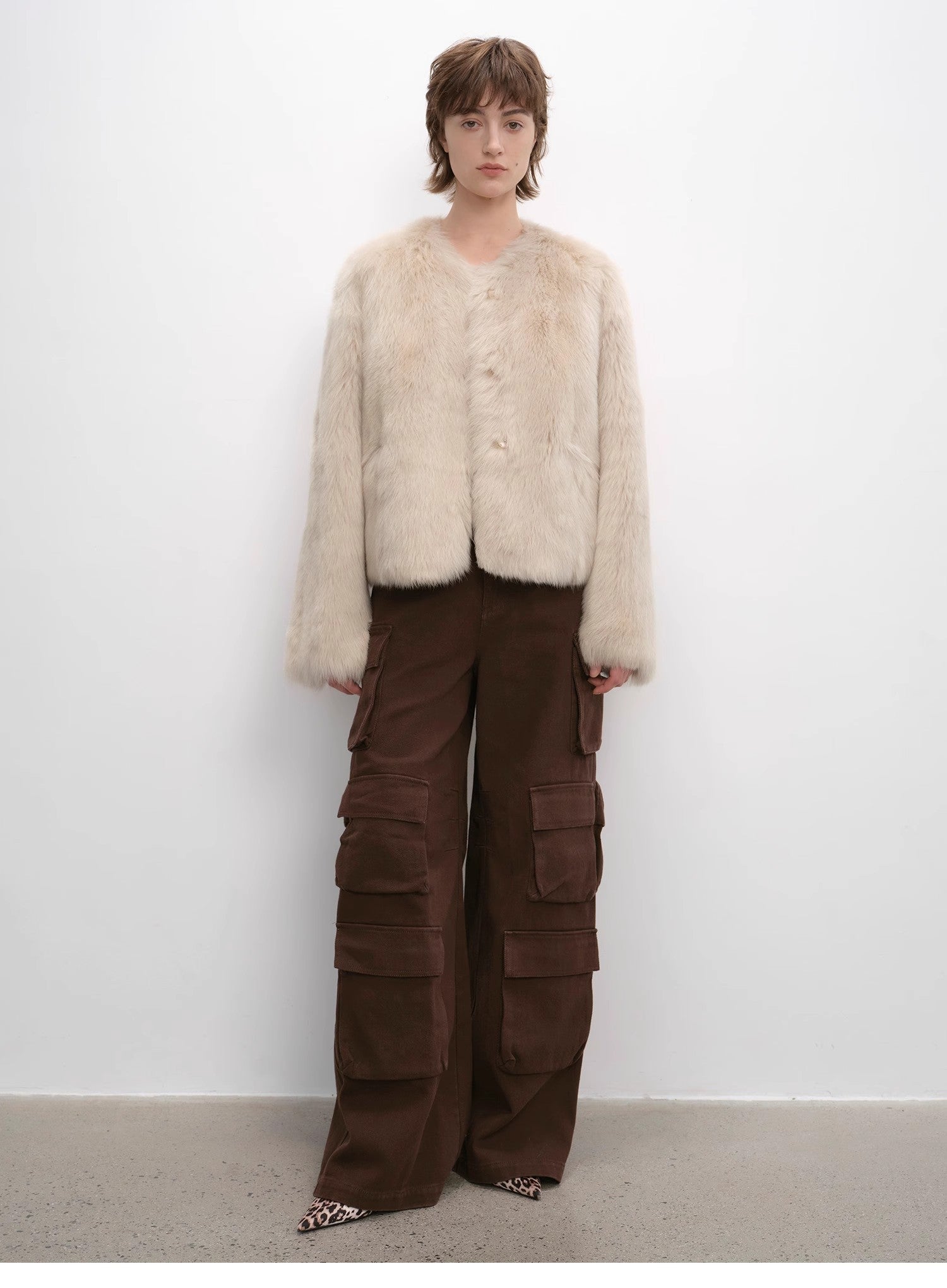 Person wearing a beige fur vest and brown cargo pants against a white background