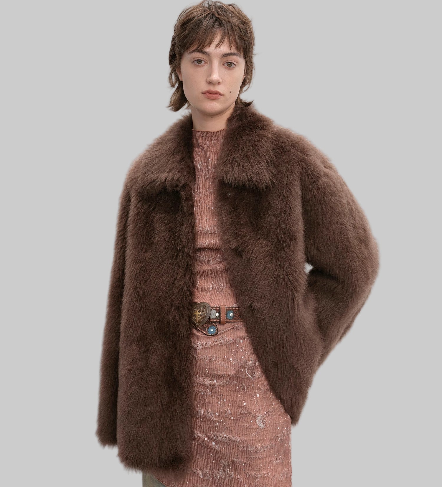 Person wearing a brown fur coat and patterned dress against a white background