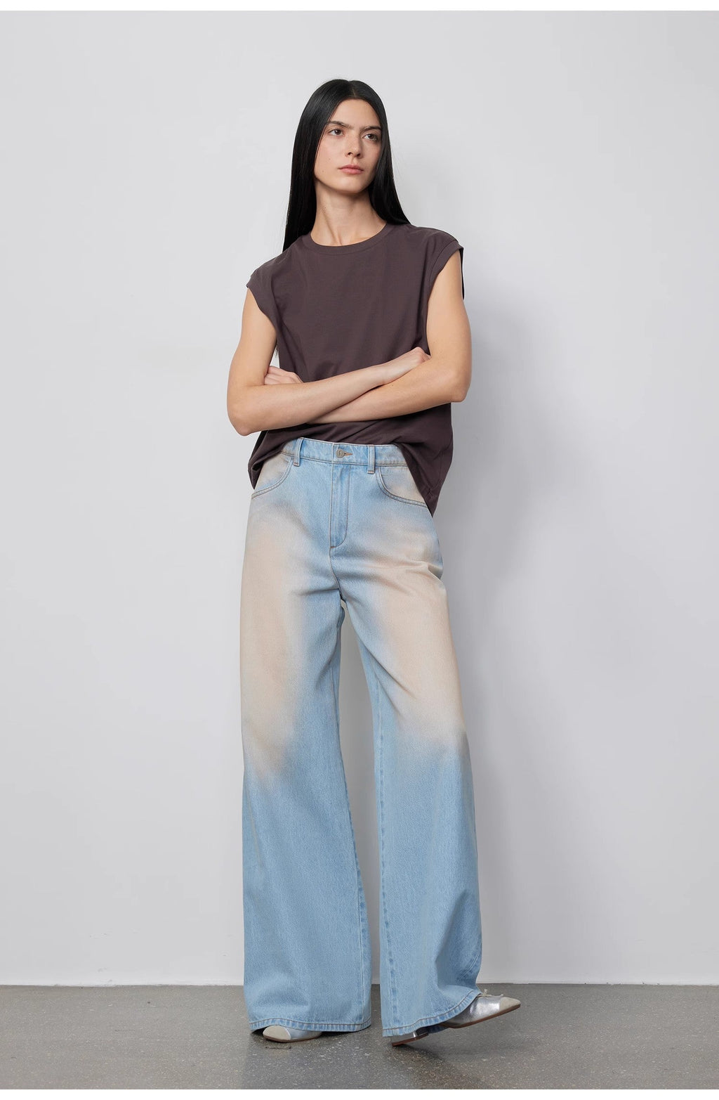 Woman wearing a sleeveless top and light blue jeans against a plain background
