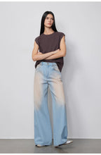 Woman wearing a sleeveless top and light blue jeans against a plain background