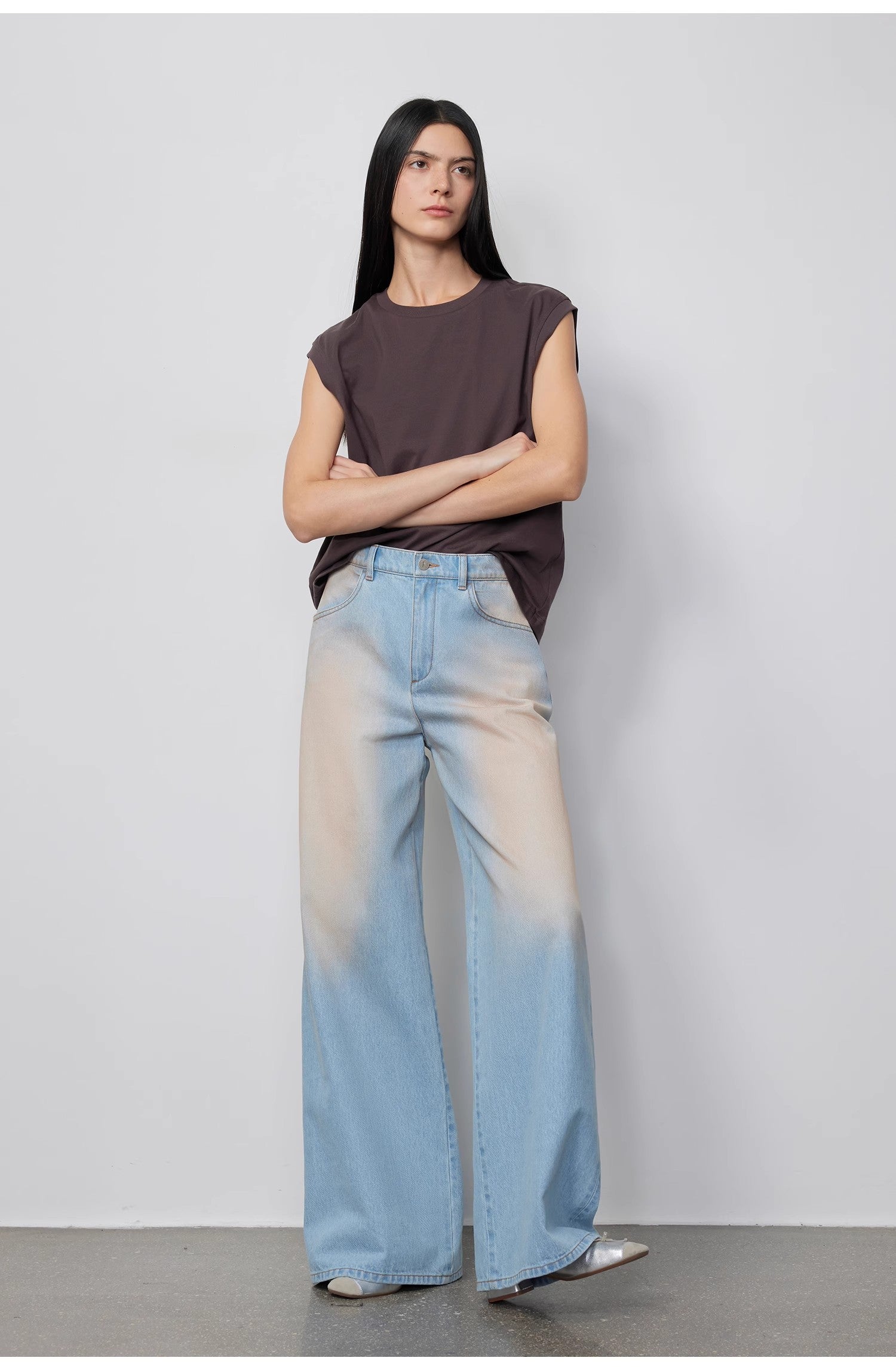 Woman wearing a sleeveless top and light blue jeans against a plain background