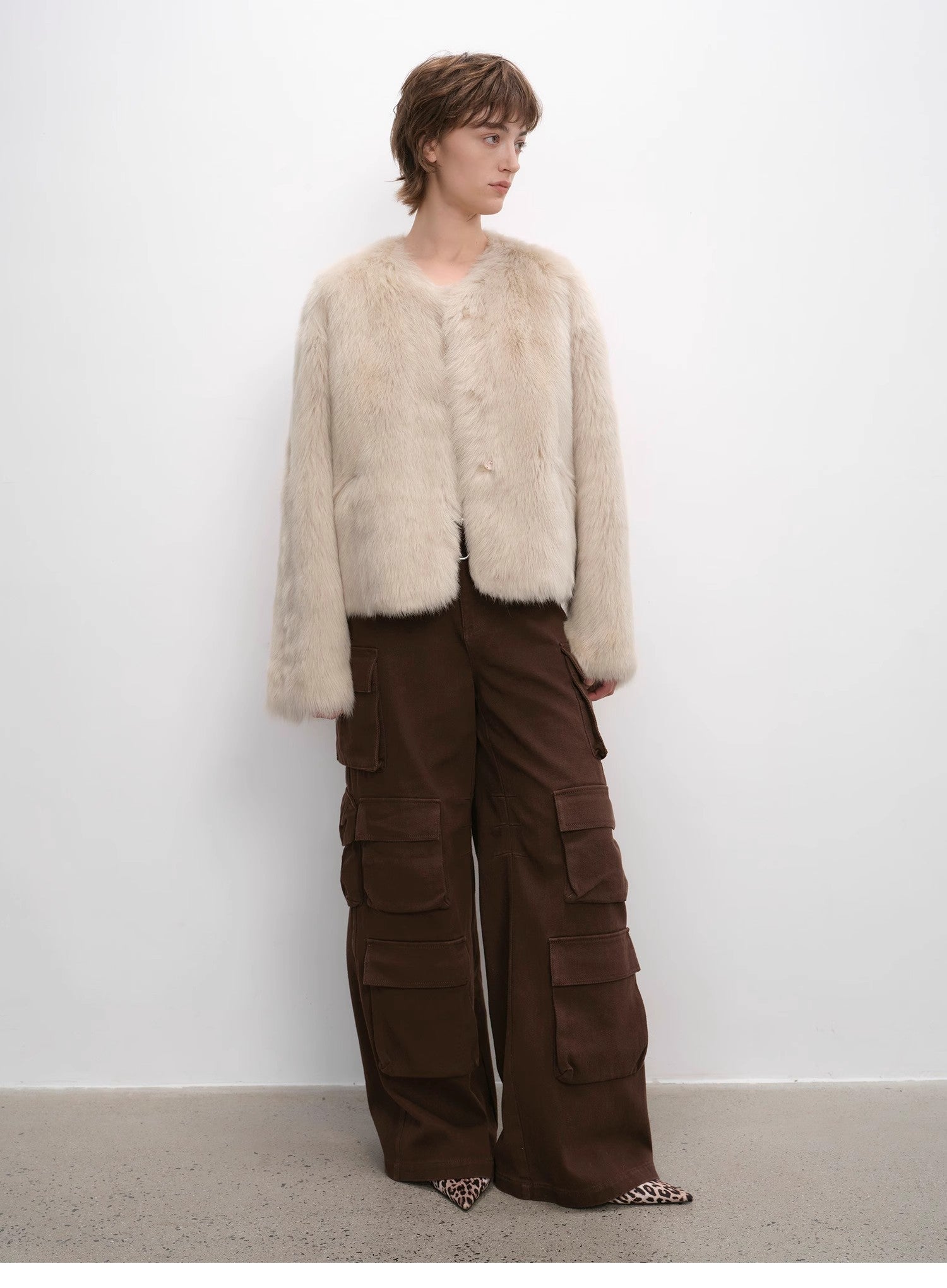 Person wearing a cream fur vest and brown cargo pants against a white background