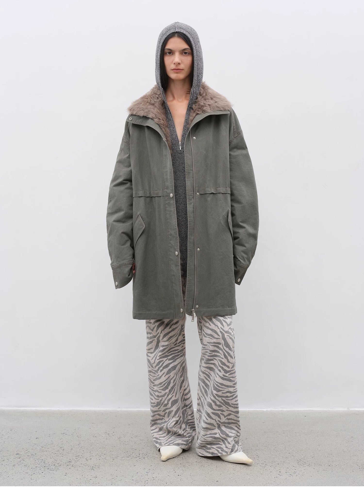 Person wearing a long green coat with a fur-lined hood against a white background