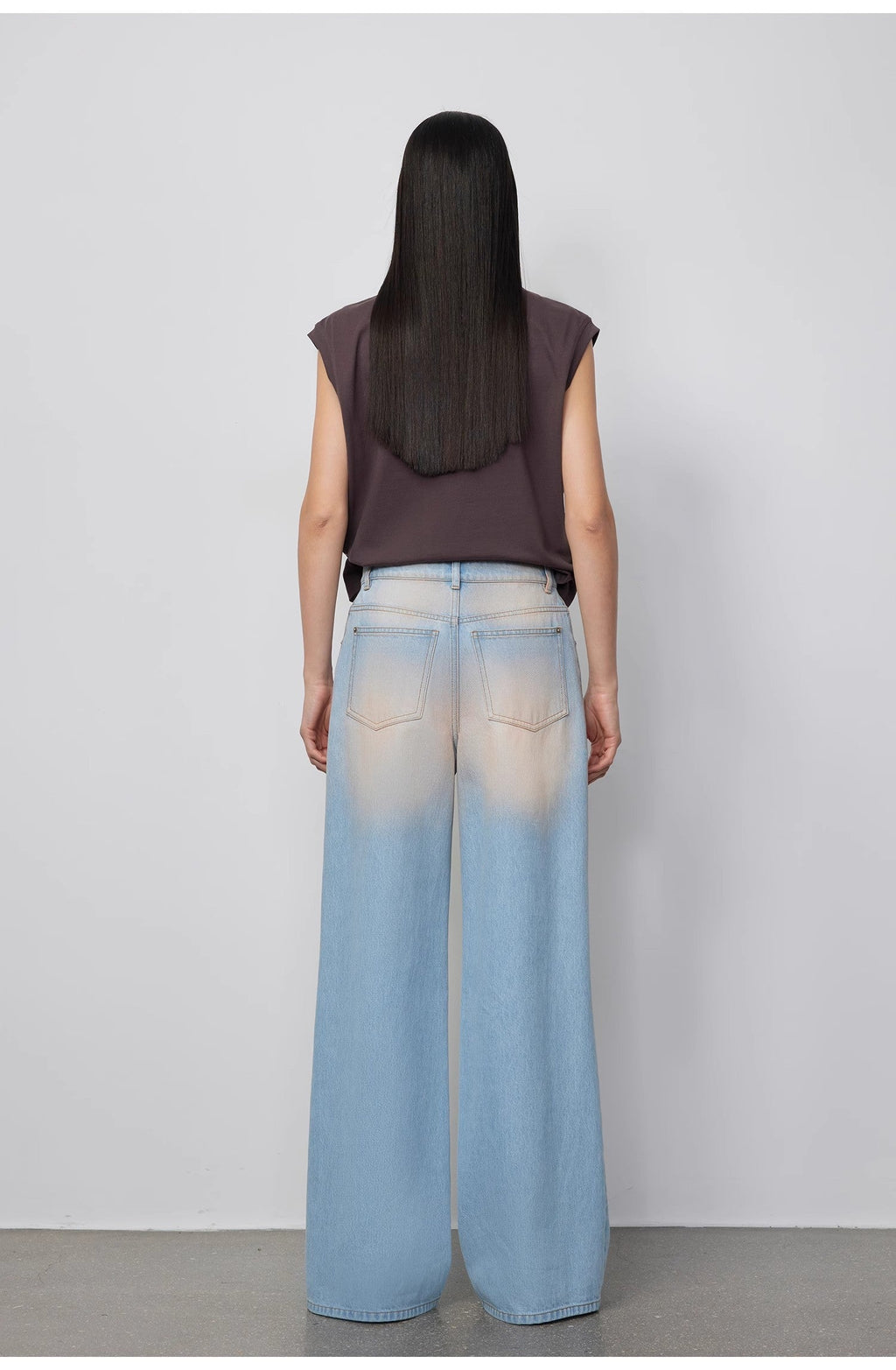 Person wearing a sleeveless top and light blue jeans against a plain background