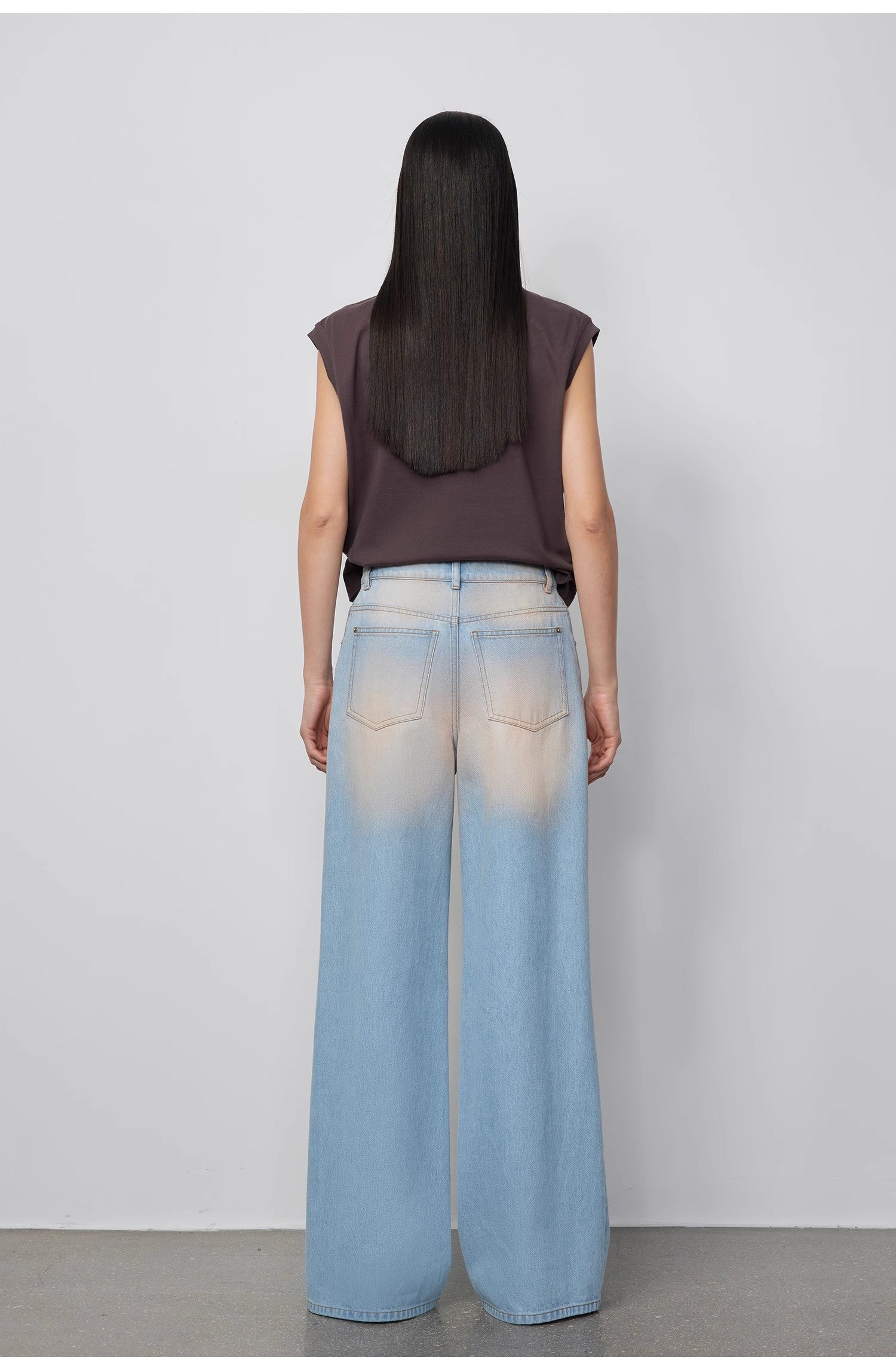 Person wearing a sleeveless top and light blue jeans against a plain background