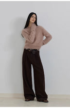 Woman wearing a pink sweater and brown wide-leg pants against a white background