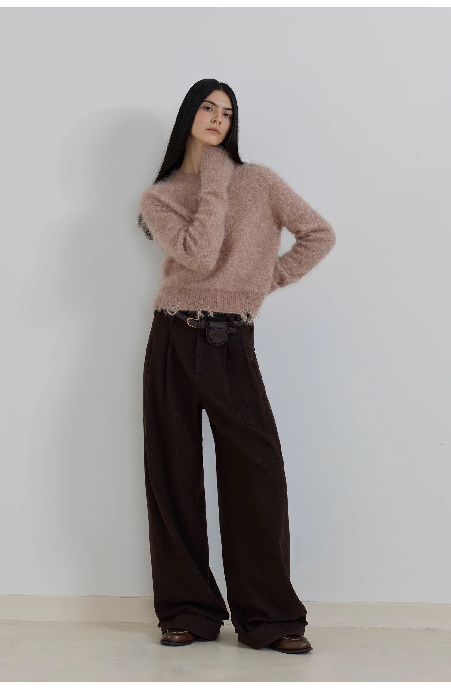 Woman wearing a pink sweater and brown wide-leg pants against a white background