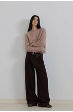 Person wearing a beige sweater and brown wide-leg pants against a plain background