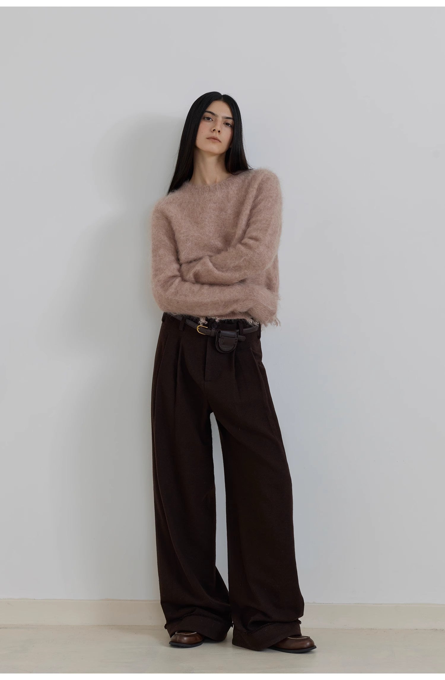 Person wearing a beige sweater and brown wide-leg pants against a plain background