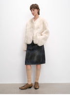Person wearing a white fur coat, denim skirt, and brown shoes against a white background
