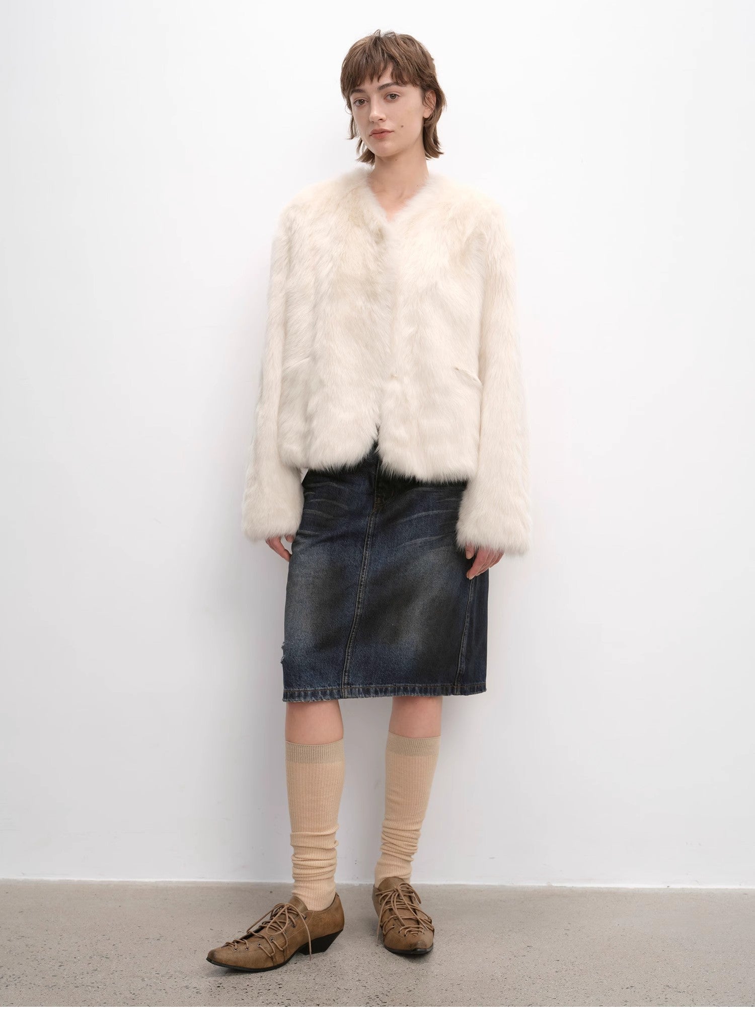 Person wearing a white fur coat, black skirt, beige knee-high socks, and brown shoes against a white background.