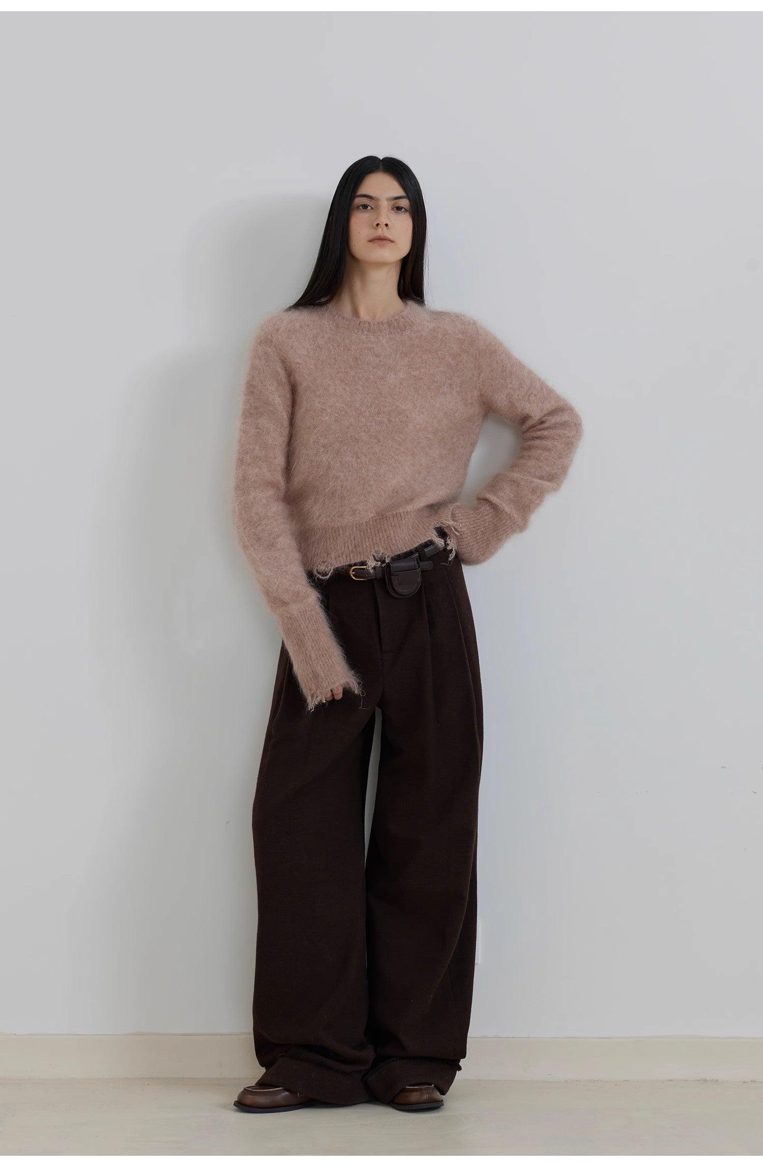 Person wearing a light pink sweater and dark brown pants against a white background