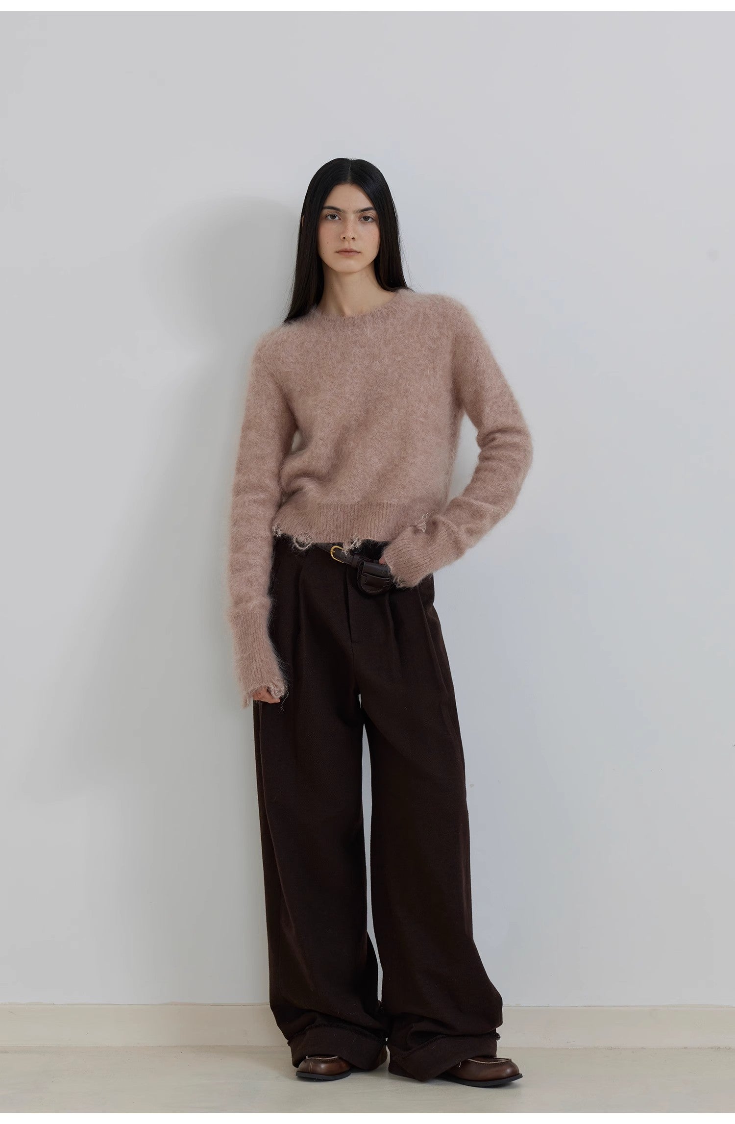 Person wearing a pink sweater and brown pants against a white background