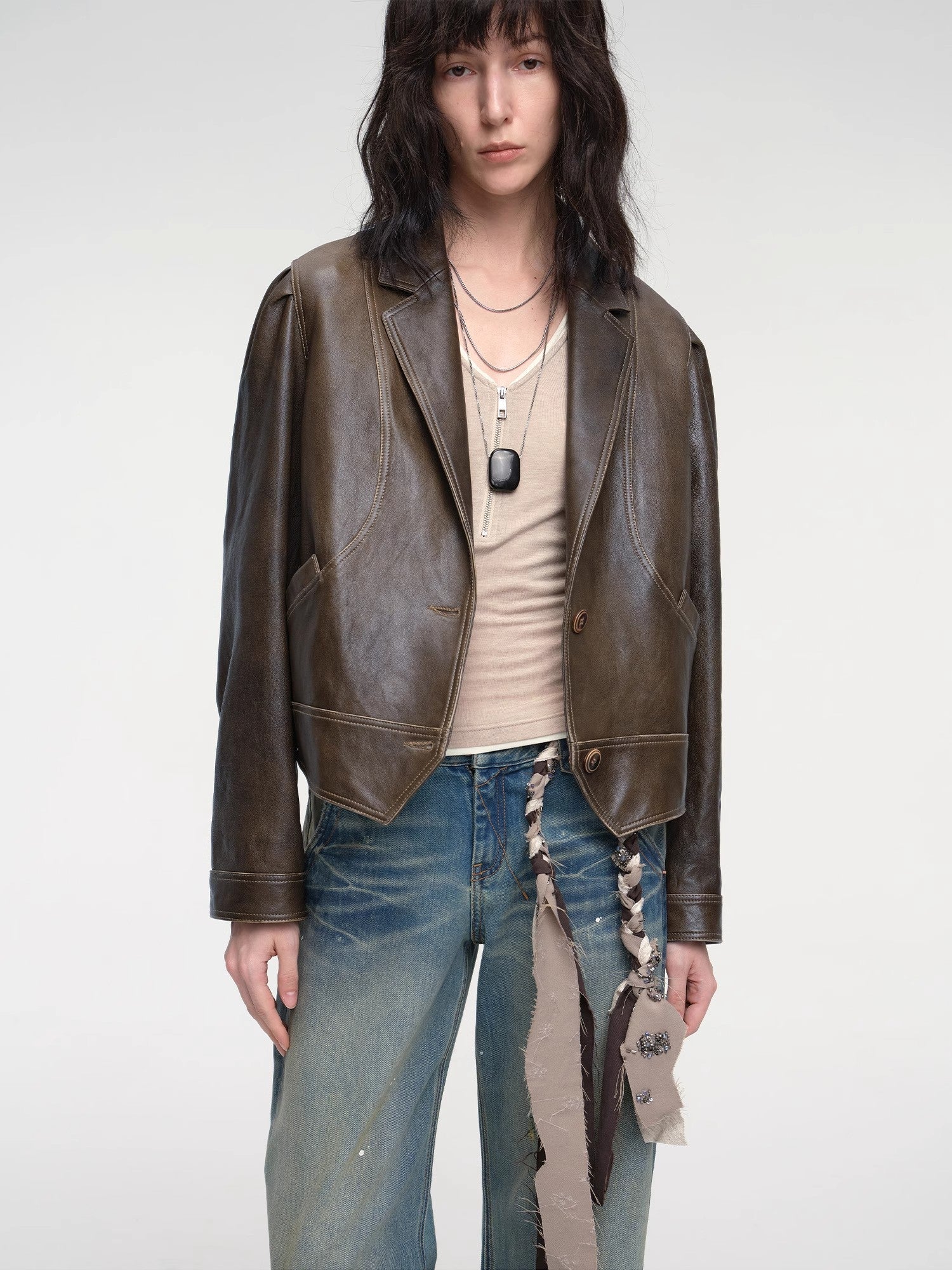 Person wearing a brown leather jacket and blue jeans on a white background