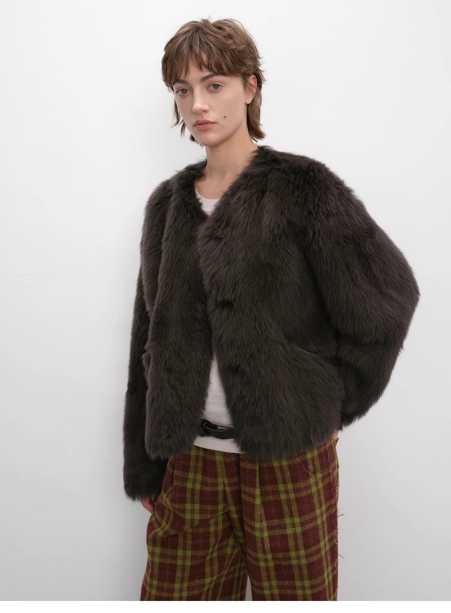 Person wearing a dark brown fur coat with plaid pants on a white background