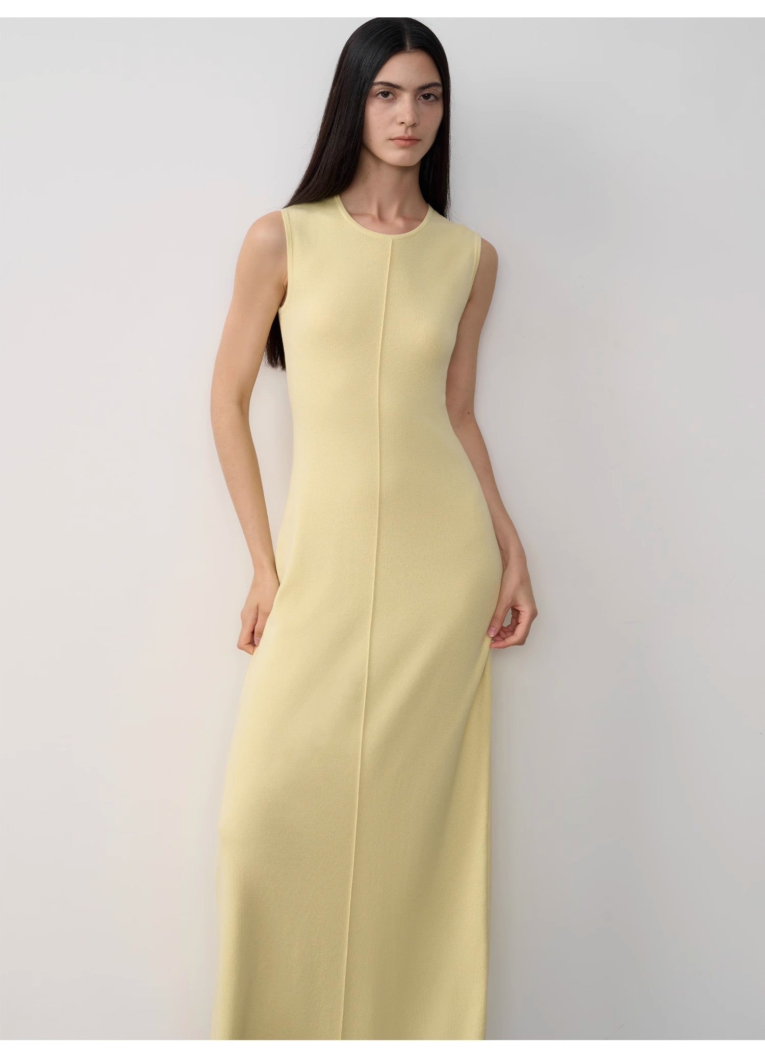 Woman wearing a light yellow sleeveless dress against a white background