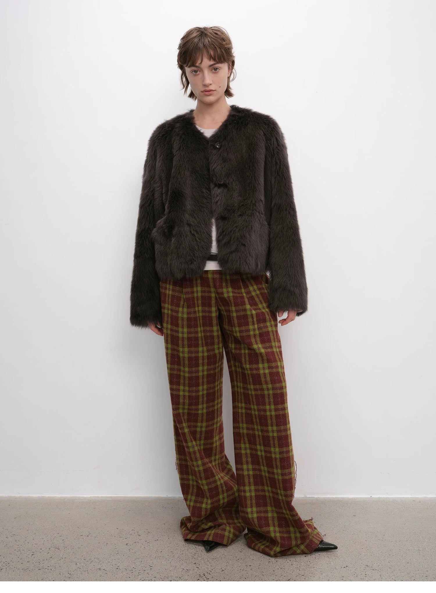 Person wearing a dark fur coat and plaid pants against a white background