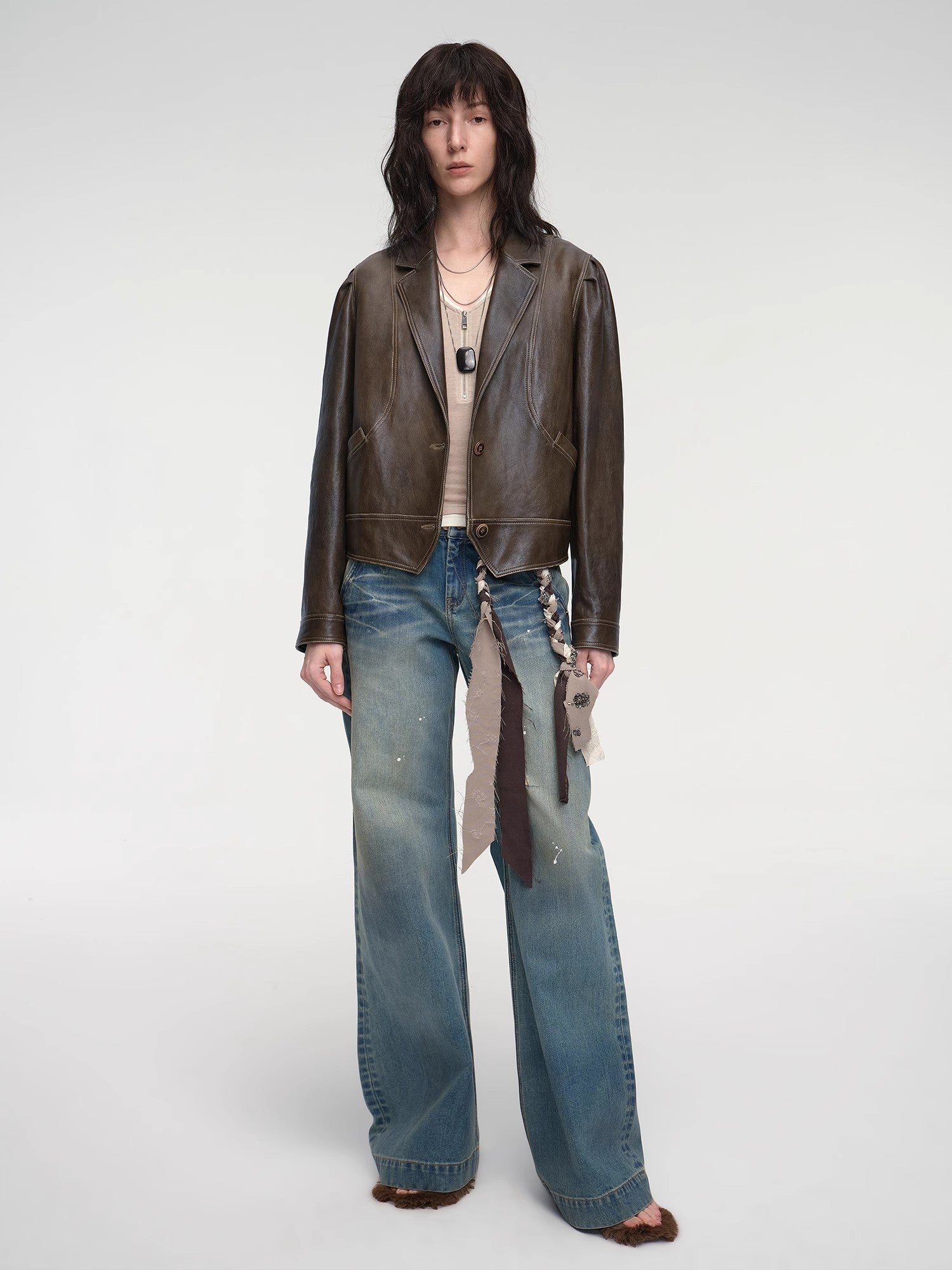 Person wearing a brown leather jacket and blue jeans on a white background