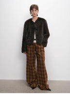 Person wearing a dark brown fur coat and plaid pants against a white background