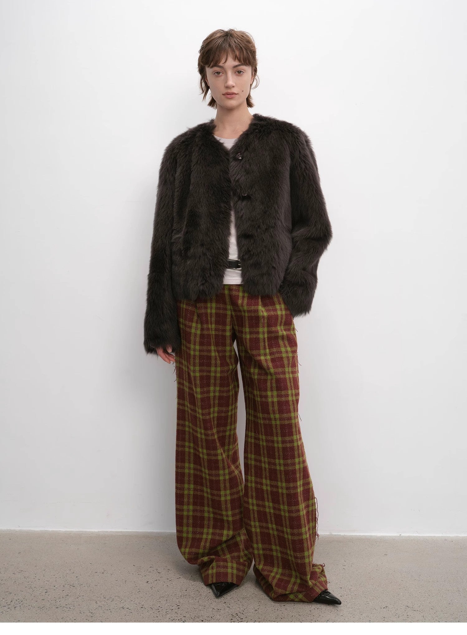 Person wearing a dark brown fur coat and plaid pants against a white background