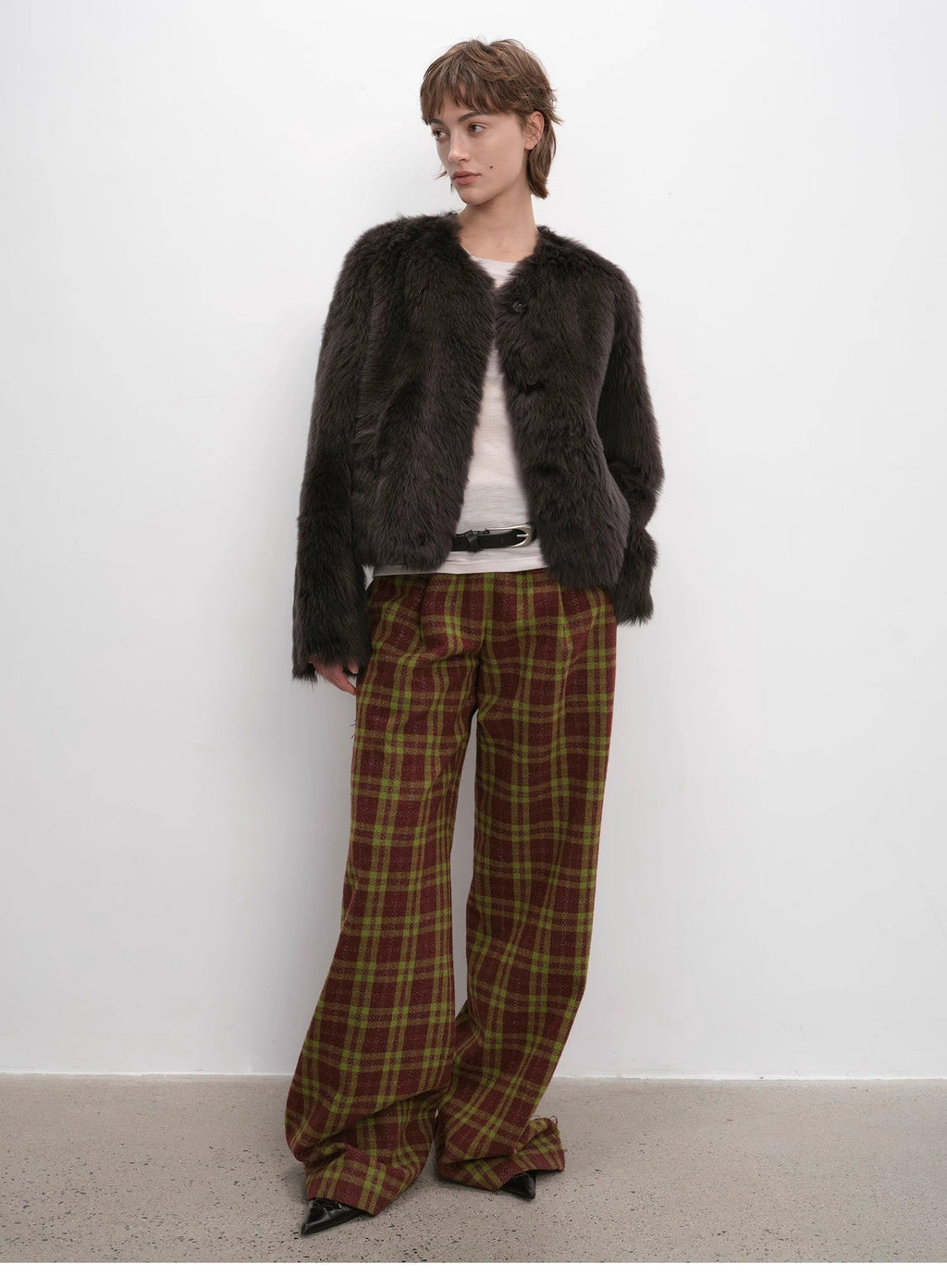 Person wearing a dark fur coat and plaid pants against a white background