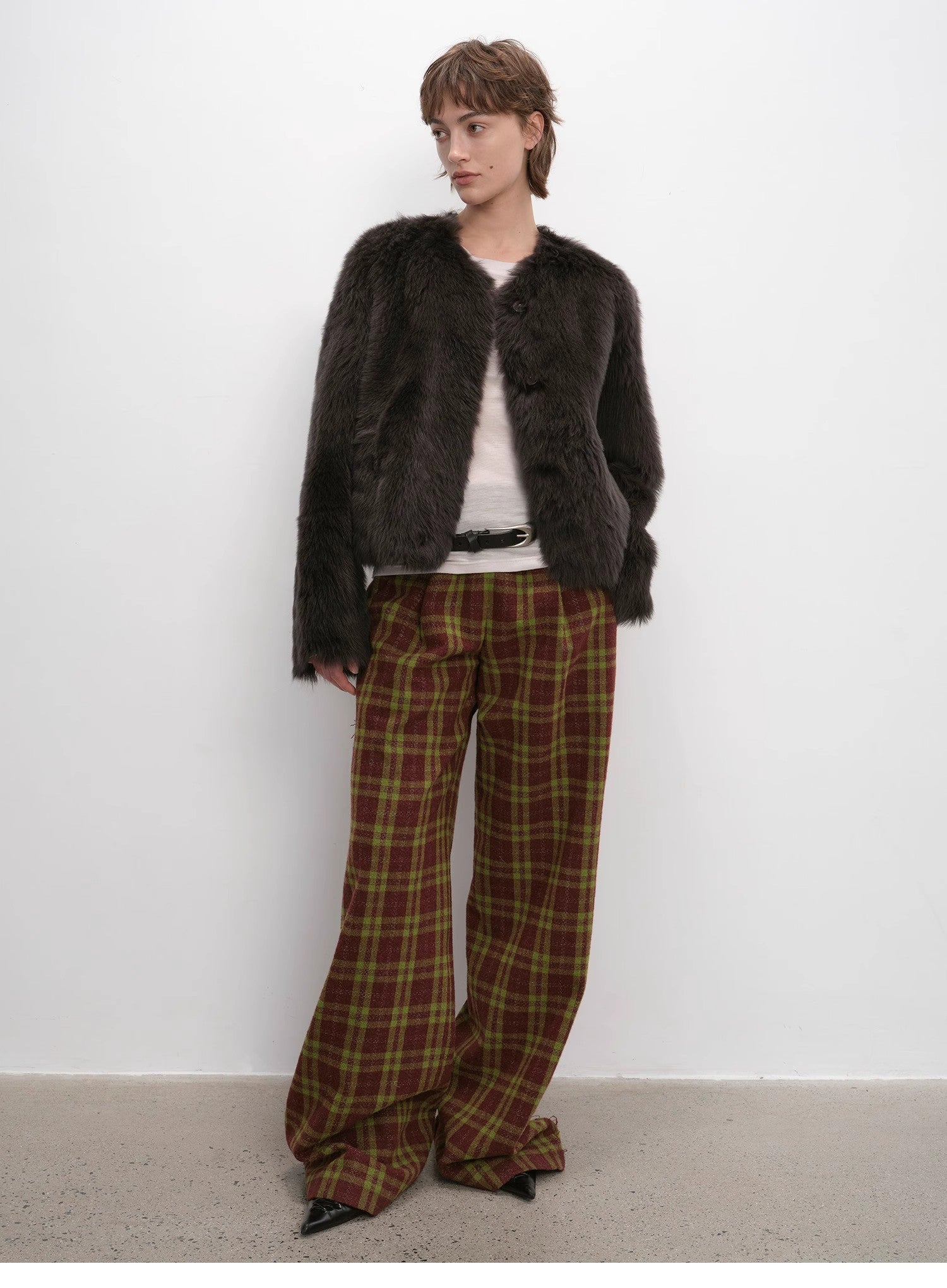 Person wearing a dark fur coat and plaid pants against a white background