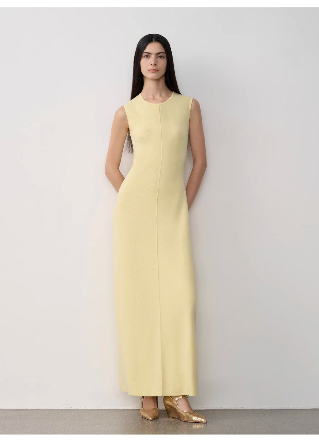 Woman wearing a light yellow sleeveless dress against a white background