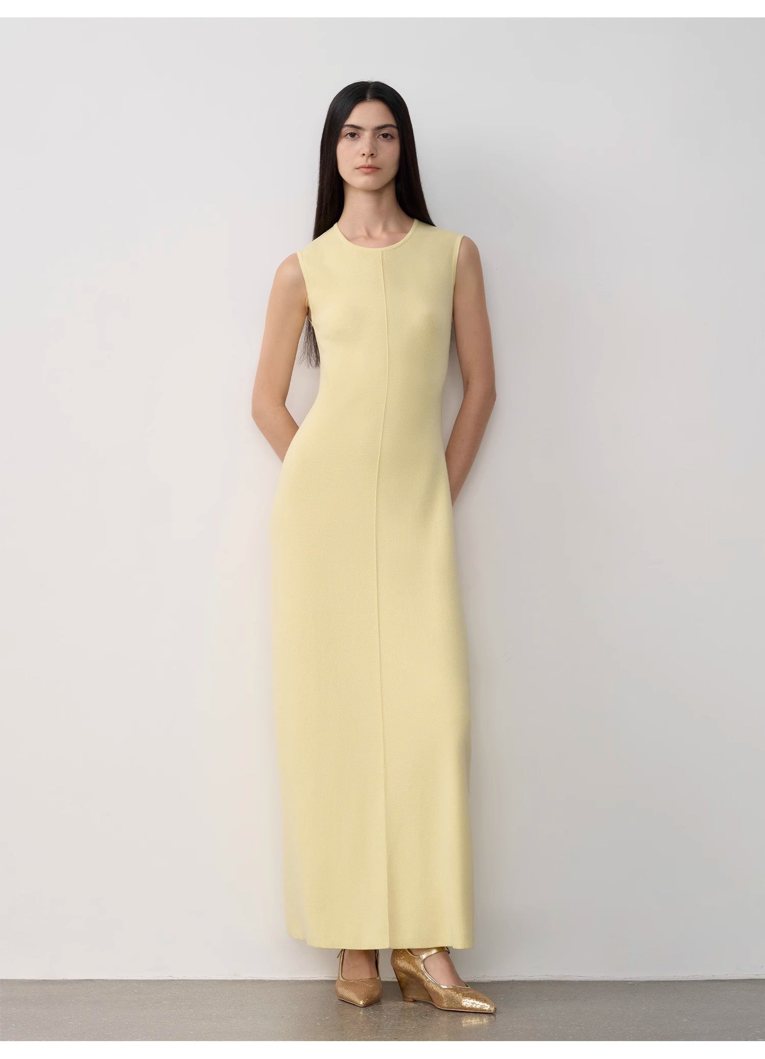 Woman wearing a light yellow sleeveless dress against a white background