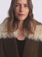 Woman wearing a brown coat with a white fur collar against a plain background