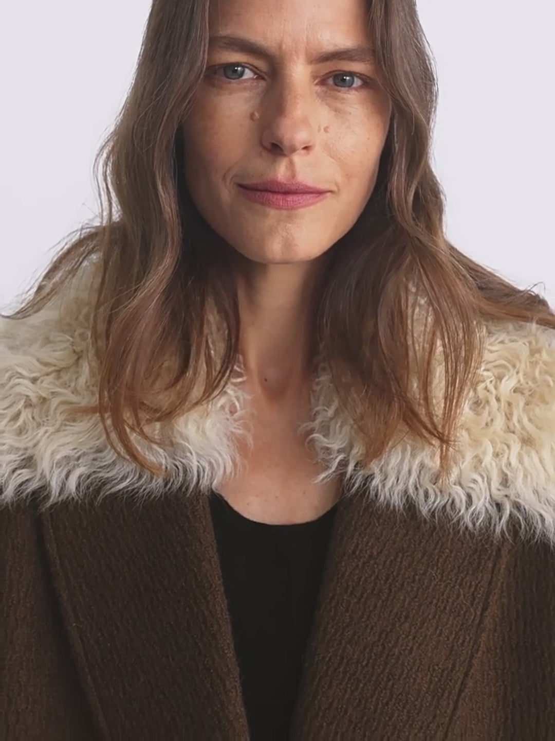Woman wearing a brown coat with a white fur collar against a plain background