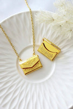 Gold necklace with a pendant shaped like a small handbag on a white plate.