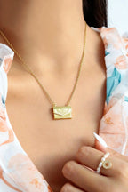 Gold necklace with a pendant worn by a person, with a blurred background.