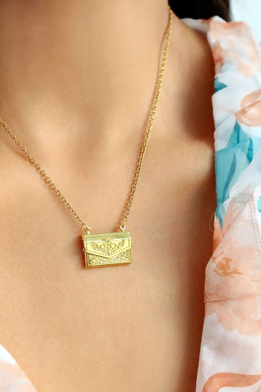 Gold necklace with a pendant on a person wearing a floral dress.