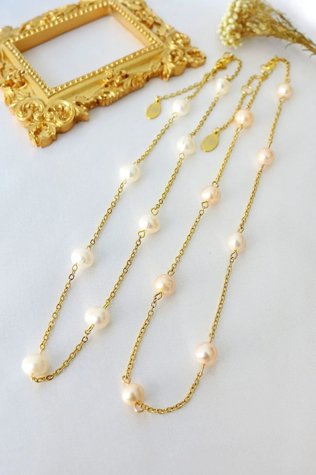 Gold chain necklace with pearls on a white surface with a gold frame in the background