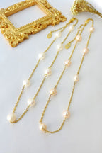 Gold chain necklace with pearls on a white surface with a gold frame in the background