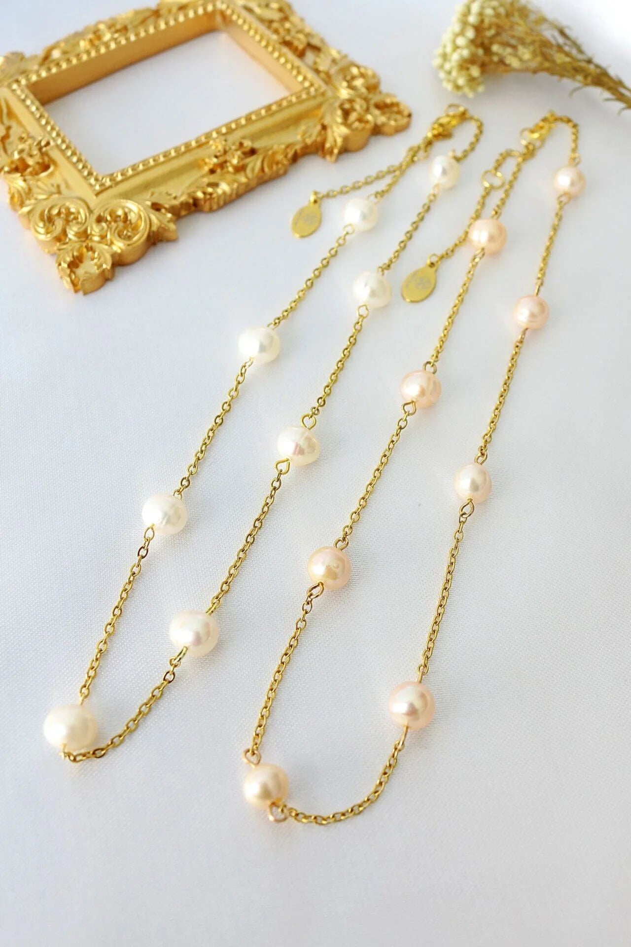 Gold chain necklace with pearls on a white surface with a gold frame in the background