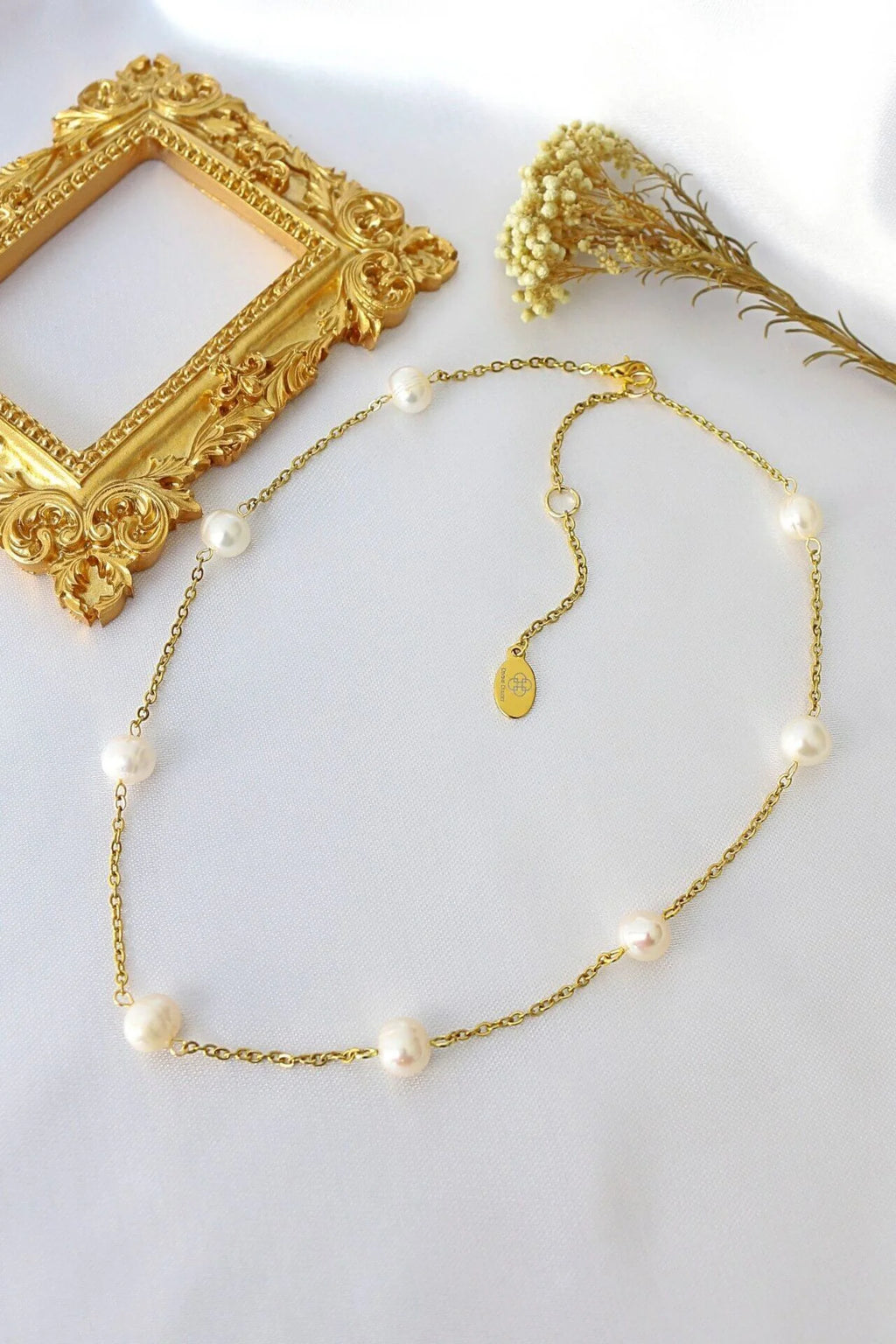 Gold necklace with pearls on a white surface with decorative elements.