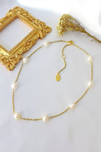 Gold necklace with pearls on a white surface with decorative elements.